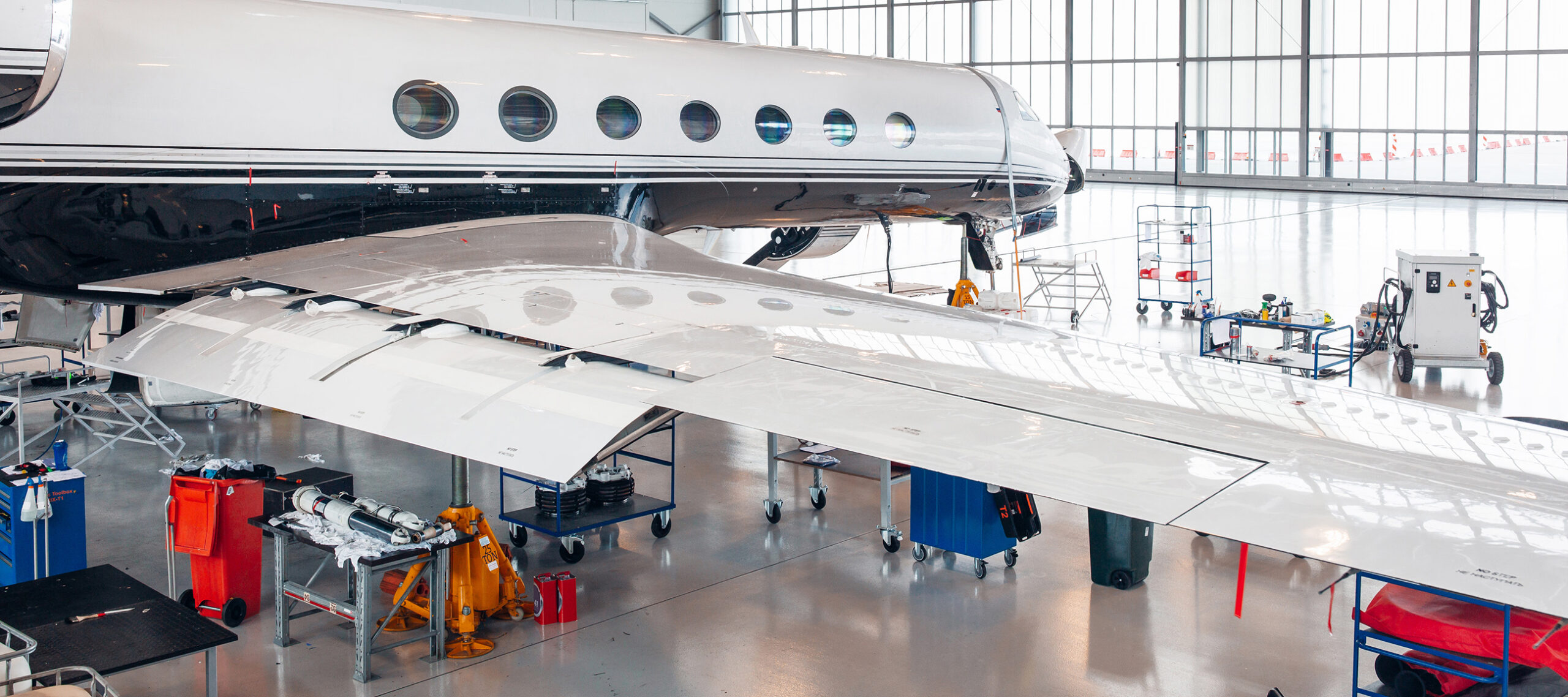 Private aircraft inside a maintenance hangar with technicians, equipment, and support operations, illustrating the complexity of aircraft management and ongoing operational oversight.