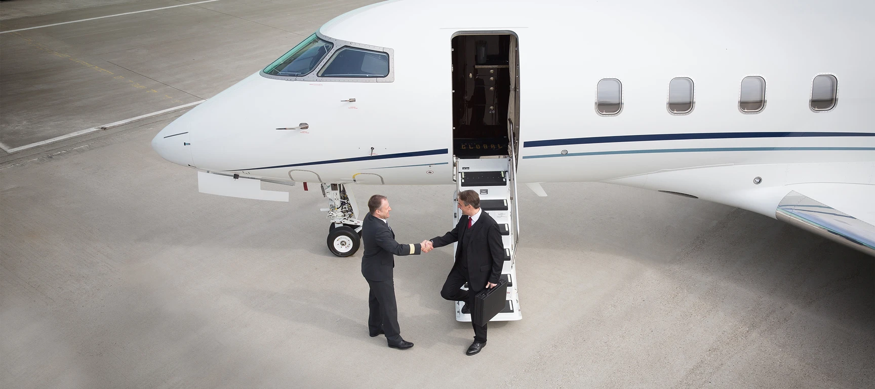 Business traveler shaking hands with a private jet pilot beside a charter aircraft, representing the trusted relationships, familiarity, and personalized service that make private aviation part of the way successful professionals do business.