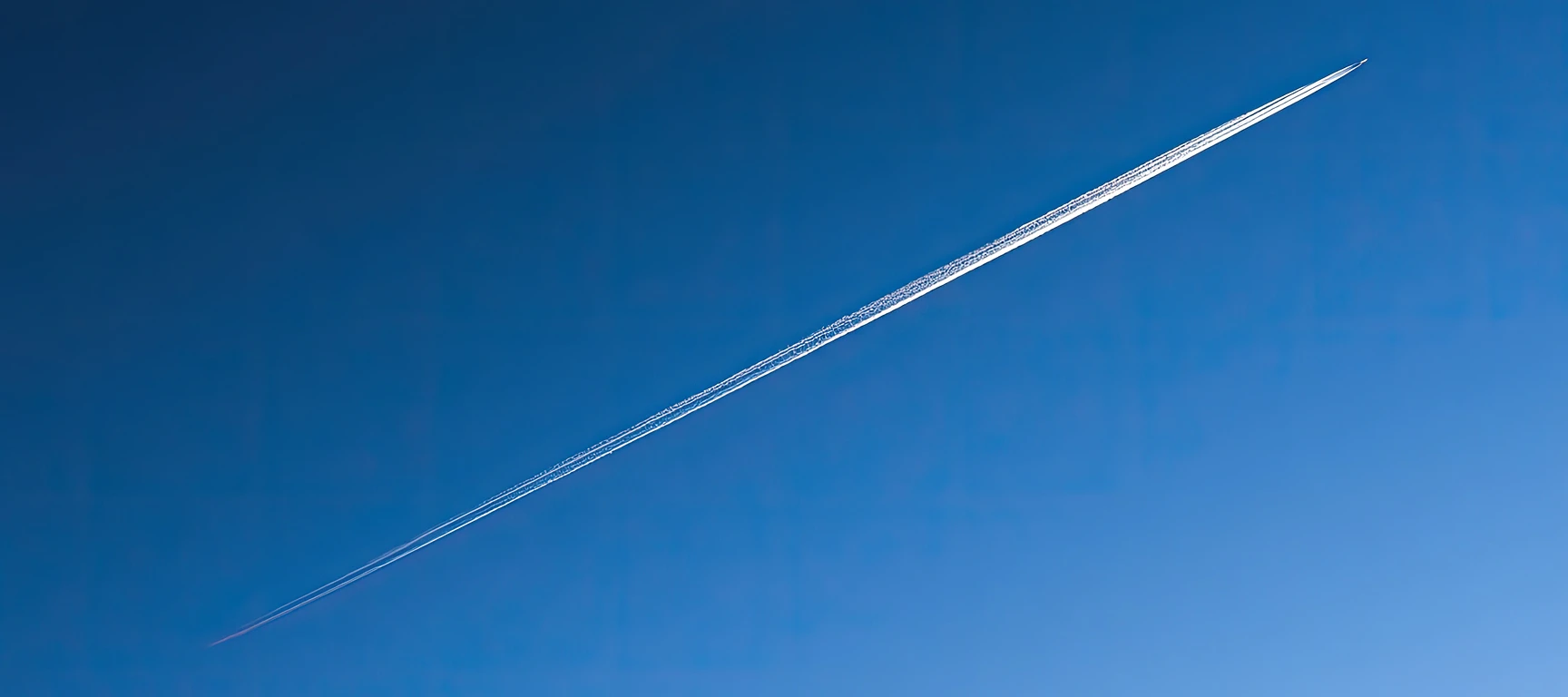 Private jet leaving a contrail across a clear blue sky, representing private aviation with the FLYUSA Jet Card.